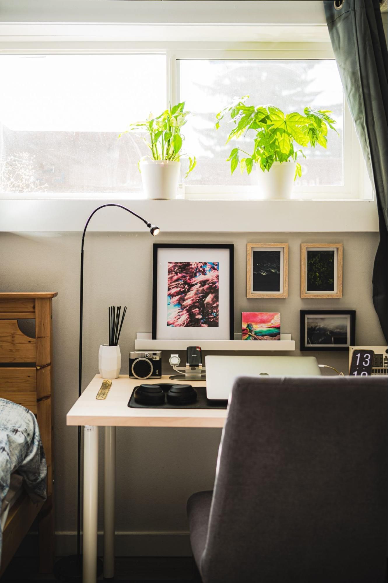 The view of room with little window, an office chair, a desk with lamp, computer, camera on it.