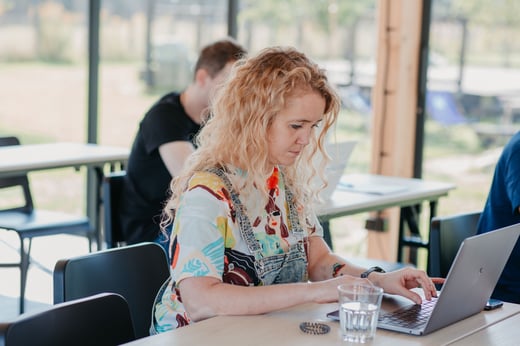 A student in denim overalls works on a laptop in a shared study area.