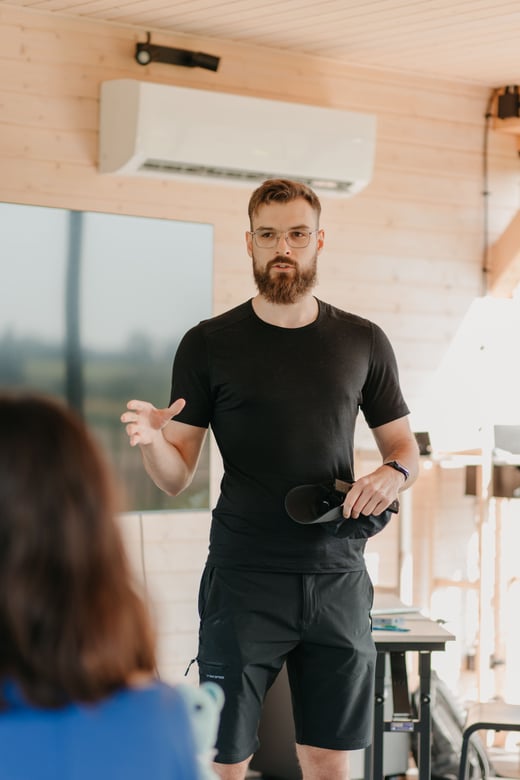 A presenter gestures while speaking in a modern wood-lined room.