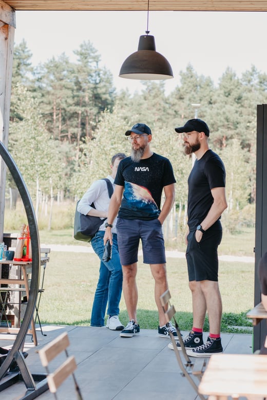 Three teammates stand together on a covered patio surrounded by pine trees.