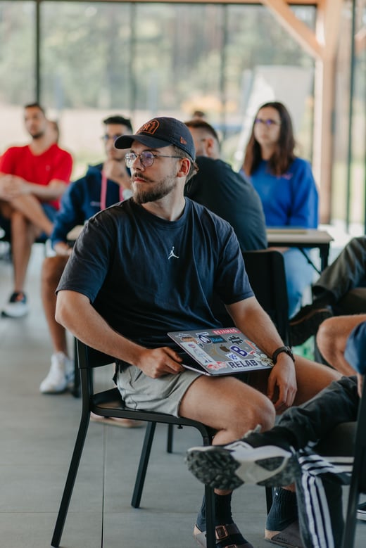 A teammate with a sticker-covered laptop listens during a presentation.