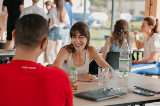 Two teammates talk across a table in a bright open space.